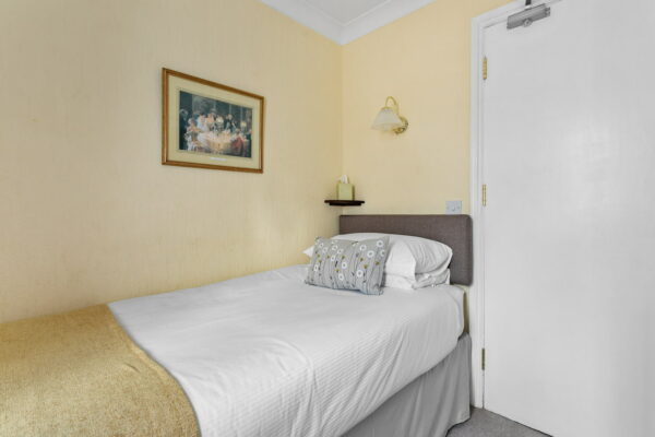 Single bedroom with yellow walls and white linen